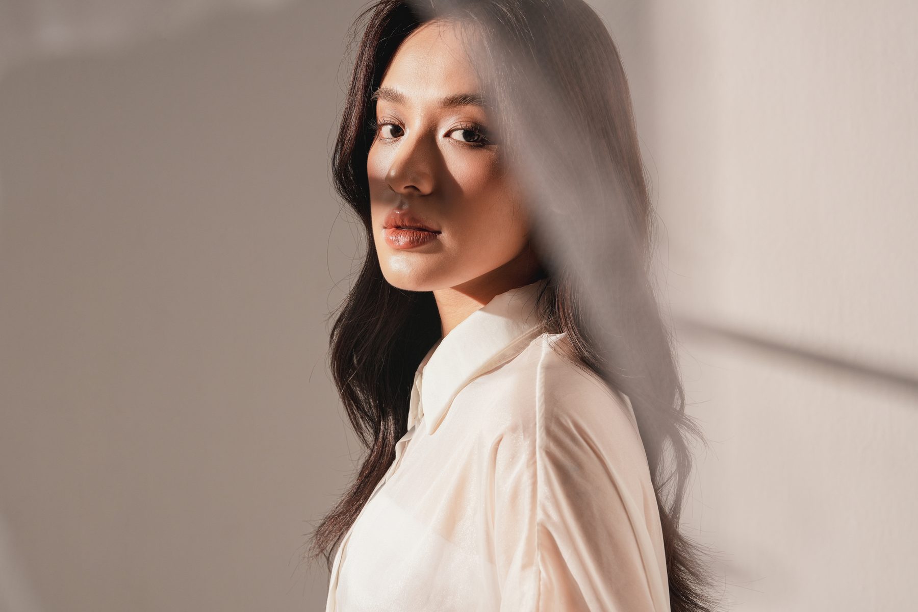 A woman in profile in sunlight against a taupe wall.